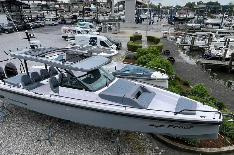Slide: The Image of 2025 Axopar 37 Sun-Top boat displayed at a marina with lush greenery. - 3