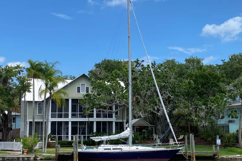 The Image of 1981 C&C 40 sailboat docked by a charming waterfront house with lush greenery. - 1