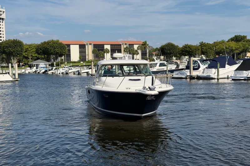 Slide: The Image of 2013 Tiara Yachts 3600 Coronet cruising in a marina with other boats docked nearby. - 7