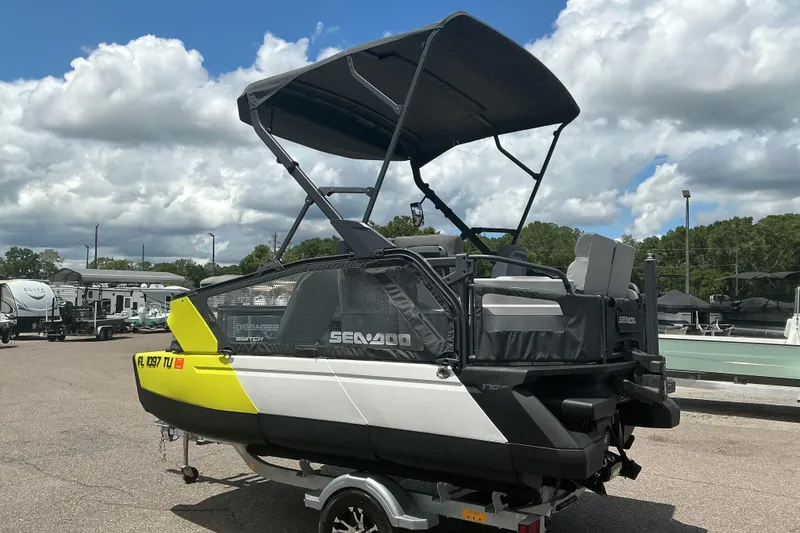 Slide: The Image of 2023 Sea-Doo Switch Sport Compact boat with canopy, parked on a trailer under cloudy skies. - 23