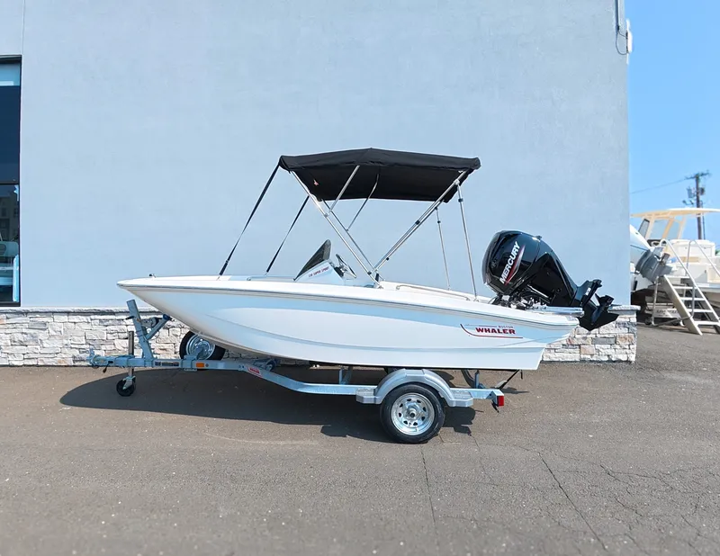 Slide: The Image of A 2027 Boston Whaler 130 Super Sport on a trailer in front of a building. - 0