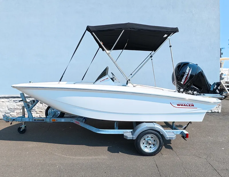 Slide: The Image of A 2027 Boston Whaler 130 Super Sport on a trailer. It features a black Bimini top. - 1