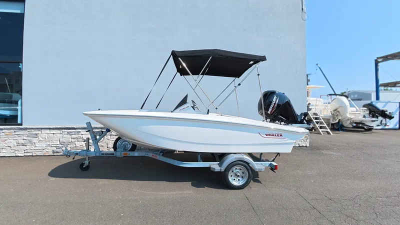 Slide: The Image of A 2027 Boston Whaler 130 Super Sport on a trailer in front of a building. - 2