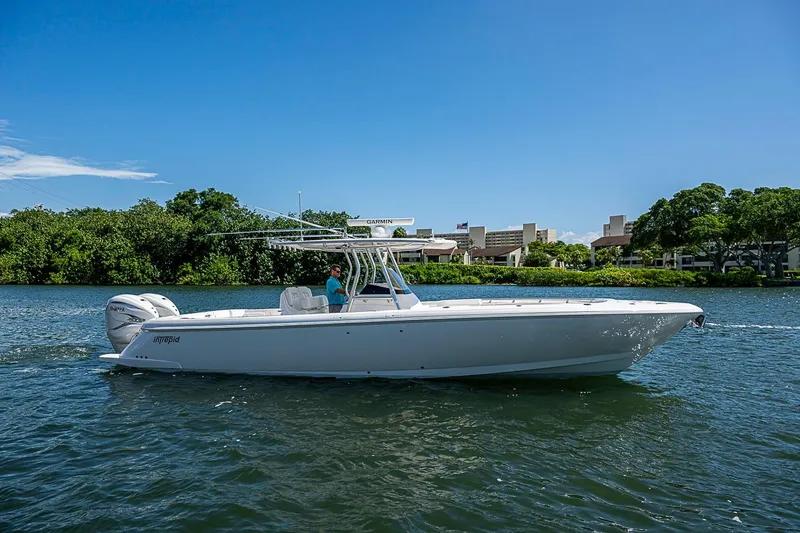 Slide: The Image of 2020 Intrepid 345 Nomad FE boat cruising on a sunny day near lush greenery. - 2