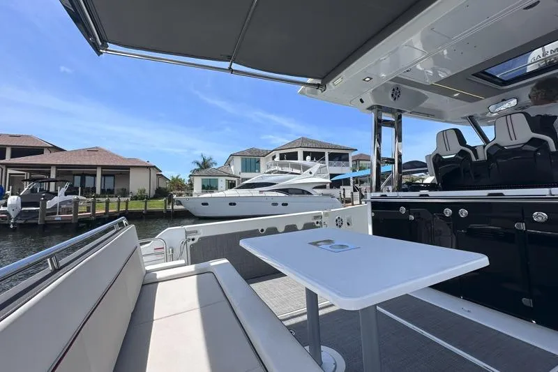 Slide: The Image of 2022 Jeanneau Leader 12.5 WA boat interior with seating and table, docked near waterfront homes. - 17