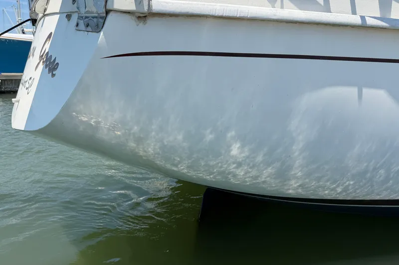 Slide: The Image of 1980 Amel Mango 52 sailboat stern reflecting sunlight on water. - 9