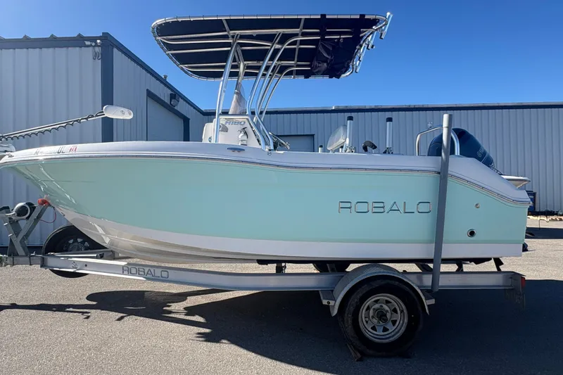 The Image of 2019 Robalo R180 Center Console boat on trailer, parked outdoors under clear blue sky. - 0