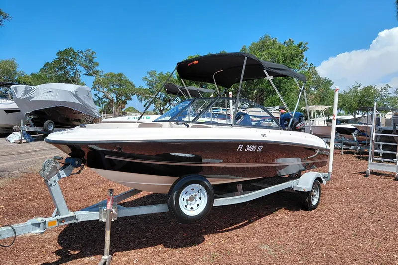 Slide: The Image of 2021 Bayliner 160 Bowrider boat on trailer, parked outdoors under clear blue sky. - 3
