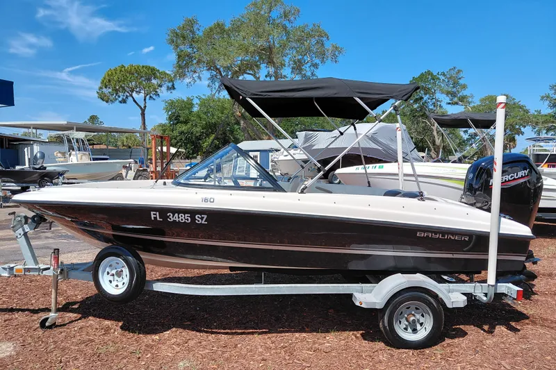 Slide: The Image of 2021 Bayliner 160 Bowrider boat on trailer, parked outdoors under clear blue sky. - 4