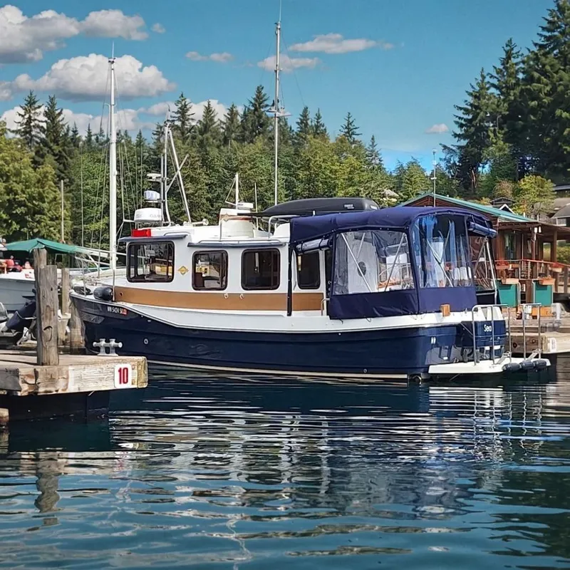 The Image of 2017 Ranger Tugs R-27 boat docked at a marina, surrounded by lush greenery. - 0