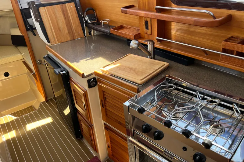 Slide: The Image of 2017 Ranger Tugs R-27 interior kitchen with stove, countertop, and wooden cabinetry. - 25