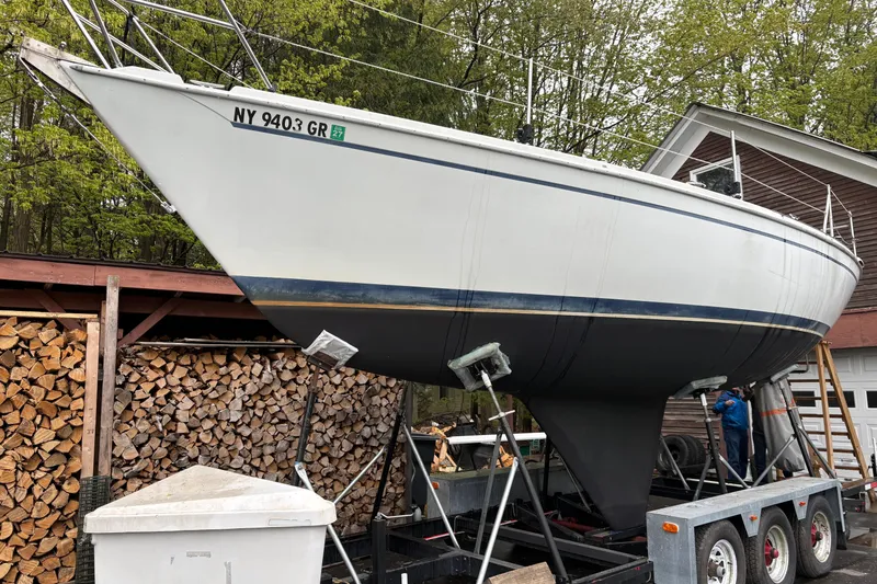 Slide: The Image of 1987 Ericson 28/2 sailboat on trailer, surrounded by stacked firewood and trees. - 3
