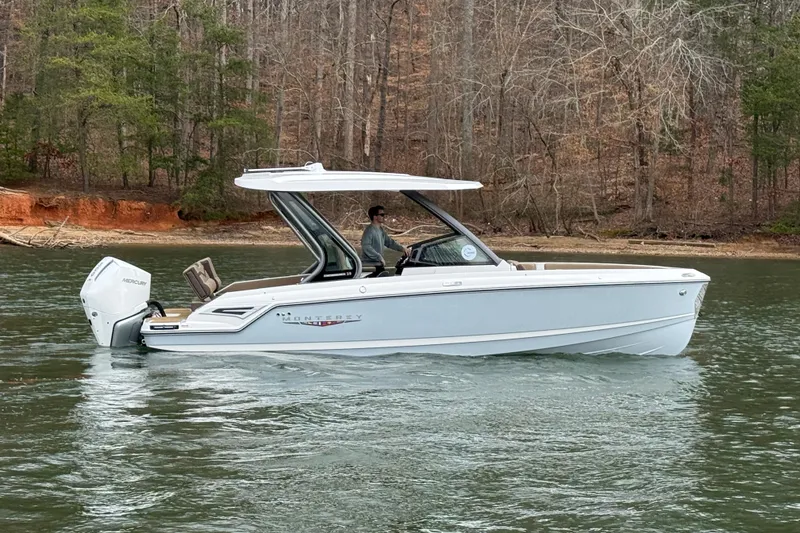Slide: The Image of 2026 Monterey Elite 25 OB boat cruising on a serene lake with wooded shoreline. - 1