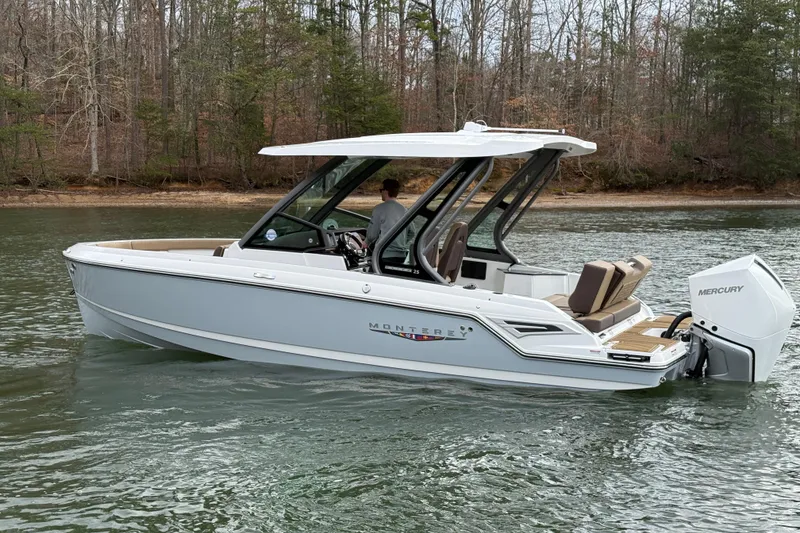 Slide: The Image of 2026 Monterey Elite 25 OB boat on a serene lake with wooded shoreline. - 5
