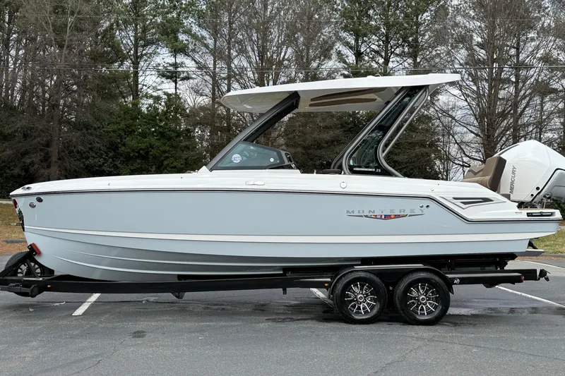 Slide: The Image of 2026 Monterey Elite 25 OB boat on trailer, parked outdoors with trees in background. - 8