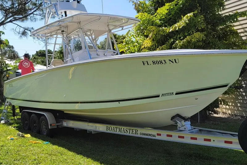 Slide: The Image of 2008 Jupiter 34 FS boat on trailer, parked outdoors, with lush greenery in the background. - 2