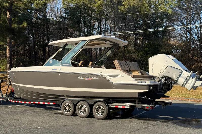 Slide: The Image of 2026 Monterey Elite 30 OB boat on trailer, parked outdoors, surrounded by trees. - 14