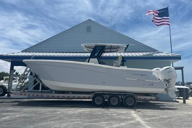 The Image of 2025 World Cat 280 CC-X boat on trailer, parked near building with American flag. - 1