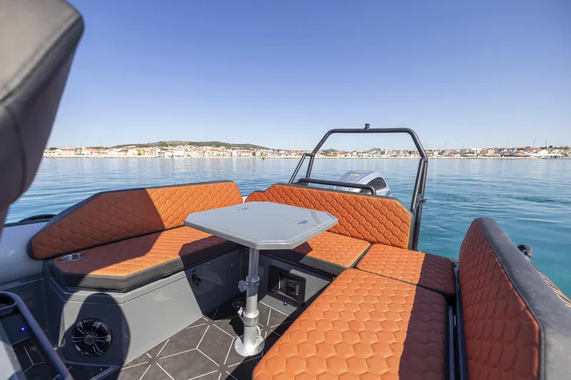 Slide: The Image of 2026 Highfield ADV7 boat interior with orange seating and table on calm water. - 9