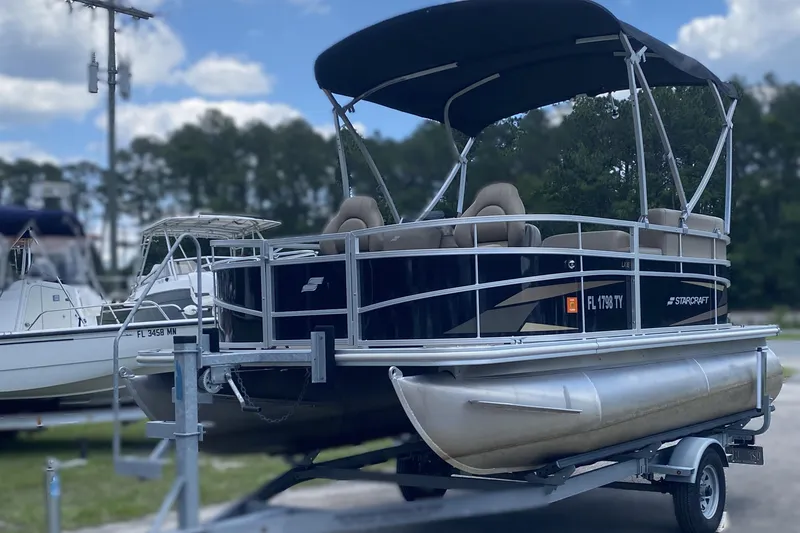 The Image of 2023 Starcraft SF 16 DLX pontoon boat on trailer, featuring canopy and seating. - 1