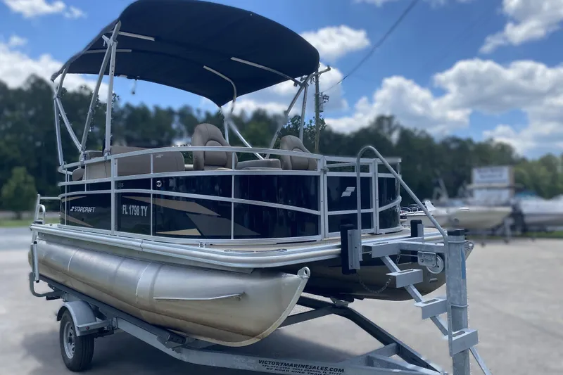 Slide: The Image of 2023 Starcraft SF 16 DLX pontoon boat on trailer, under blue sky. - 2