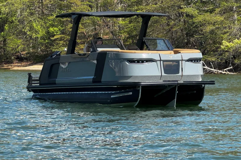 Slide: The Image of 2026 Revel RS25L pontoon boat on a serene lake, surrounded by lush greenery. - 1