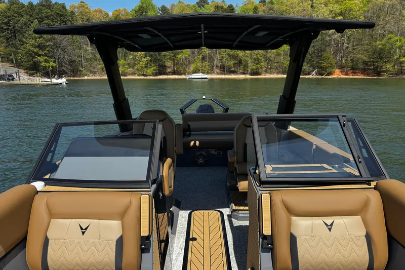 Slide: The Image of 2026 Revel RS25L boat interior with tan seats and glass windshields on a scenic lake. - 15