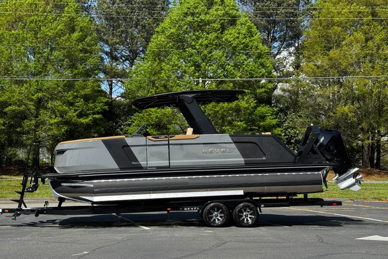 Slide: The Image of 2026 Revel RS25L luxury boat on trailer, parked outdoors with lush green trees in background. - 18