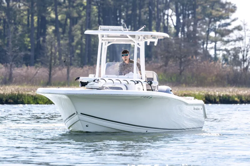Slide: The Image of 2021 Tidewater 220 LXF boat cruising on a serene lake with forest backdrop. - 6
