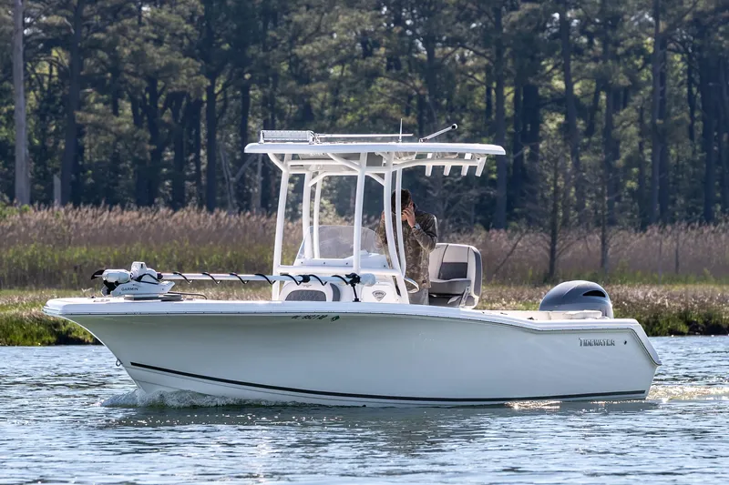 Slide: The Image of 2021 Tidewater 220 LXF boat cruising on a serene waterway with forest backdrop. - 7