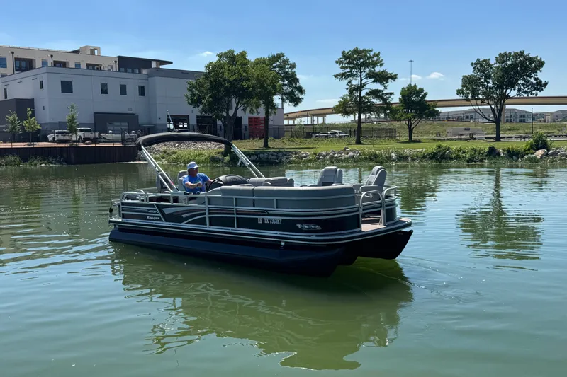 Slide: The Image of 2022 Ranger 223FC pontoon boat on a calm lake near modern buildings and trees. - 3