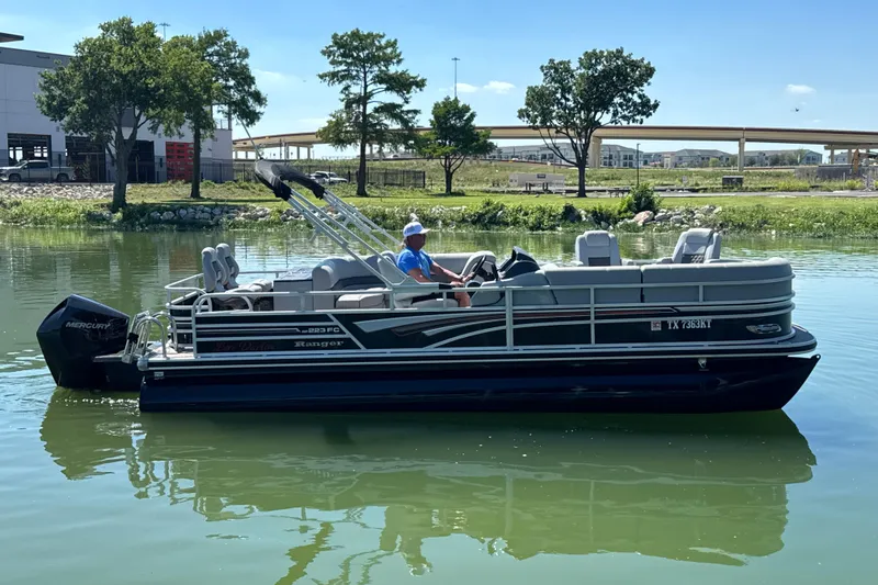 Slide: The Image of 2022 Ranger 223FC pontoon boat on a calm lake with trees in the background. - 4