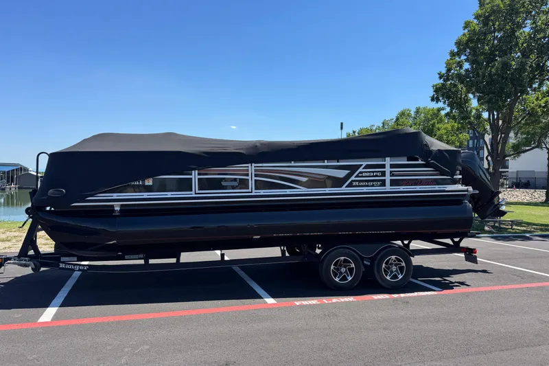 Slide: The Image of 2022 Ranger 223FC pontoon boat on trailer, covered, parked near a lake. - 6