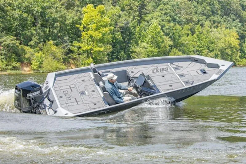 The Image of A 2026 Excel EX 203 boat navigating a lake with lush green trees in the background. - 1