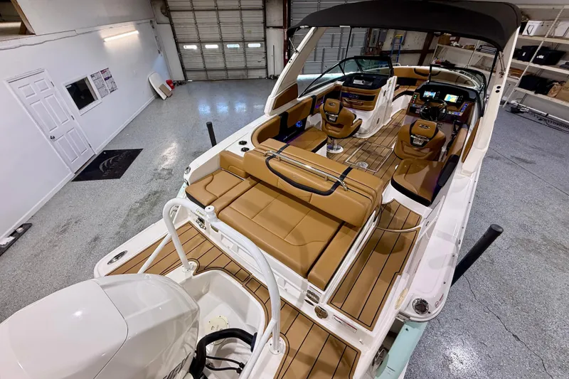 Slide: The Image of 2023 Chaparral 270 OSX boat interior with tan seating and modern dashboard in a garage setting. - 16