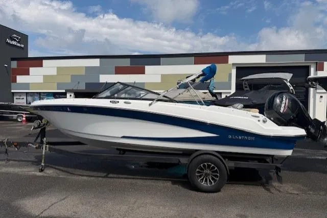 The Image of 2022 Glastron GX 210 Sport boat on trailer, parked outside dealership under cloudy sky. - 0