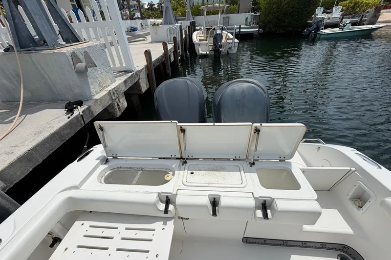 Slide: The Image of 2004 Triton 2895 CC boat with open storage compartments, docked by the water. - 21