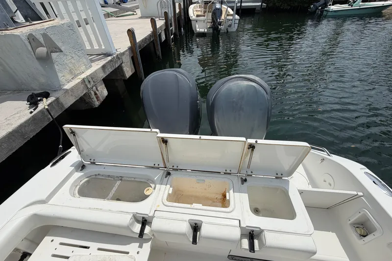 Slide: The Image of 2004 Triton 2895 CC boat with open storage compartments and dual outboard motors at dock. - 22