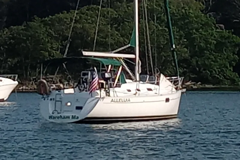 The Image of Sailboat "Alleluia," Beneteau Oceanis 321, 1995, anchored in calm waters with lush greenery. - 0