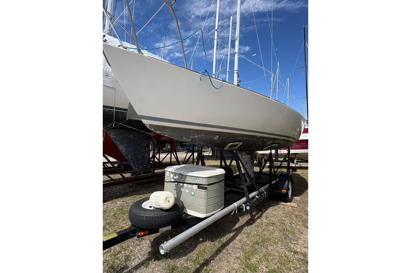 The Image of 1982 J Boats J/24 sailboat on trailer, parked outdoors under clear blue sky. - 1