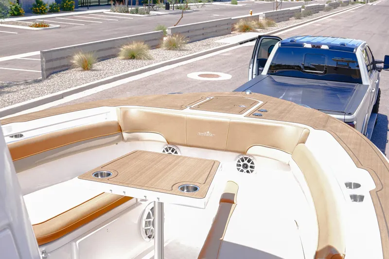 Slide: The Image of 2024 NauticStar 292 Legacy boat interior with seating and table, parked near a truck. - 2