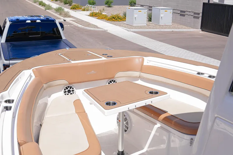 Slide: The Image of 2024 NauticStar 292 Legacy boat interior with tan seating and table, parked near a blue truck. - 3