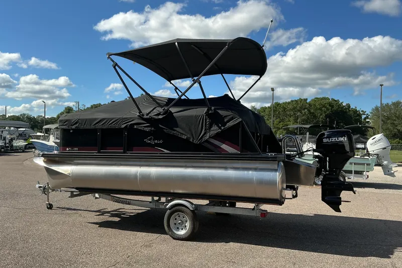Slide: The Image of 2025 Qwest E-Class RLS 16 pontoon boat with Suzuki outboard motor, parked outdoors. - 2