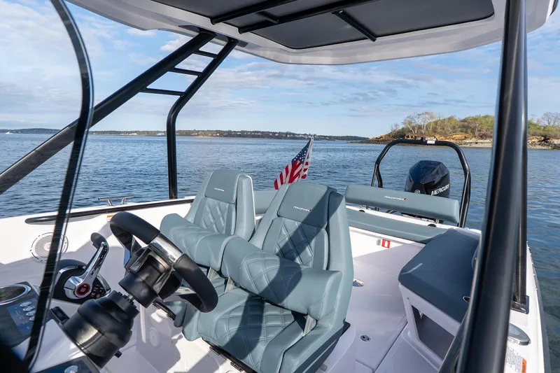 Slide: The Image of 2025 Axopar Cross Top boat interior with steering wheel, seats, and American flag on a calm lake. - 14