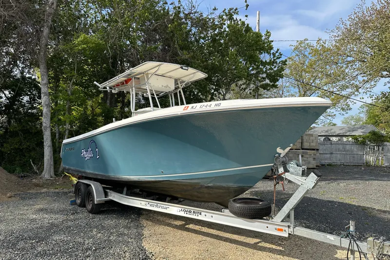 Slide: The Image of 2011 Sailfish 2660 CC boat on trailer, parked outdoors with trees in background. - 6