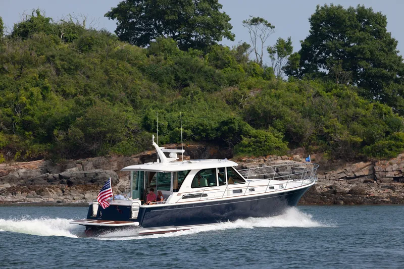Slide: The Image of 2026 Sabre 45 Salon Express yacht cruising near lush, rocky shoreline. - 1