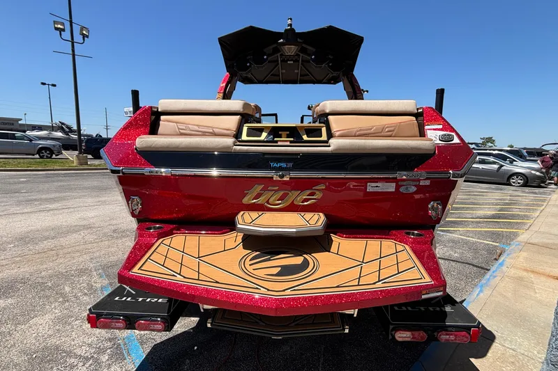 Slide: The Image of 2026 Tigé Ultré 25ZX boat with red exterior and tan seating, parked outdoors. - 3
