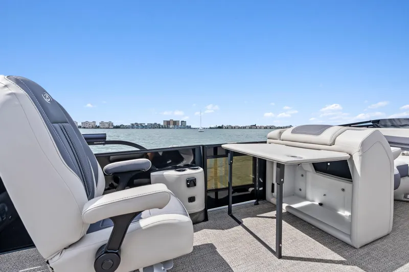 Slide: The Image of 2025 Barletta Corsa 23UC boat interior with seating and table, overlooking a scenic waterfront. - 10