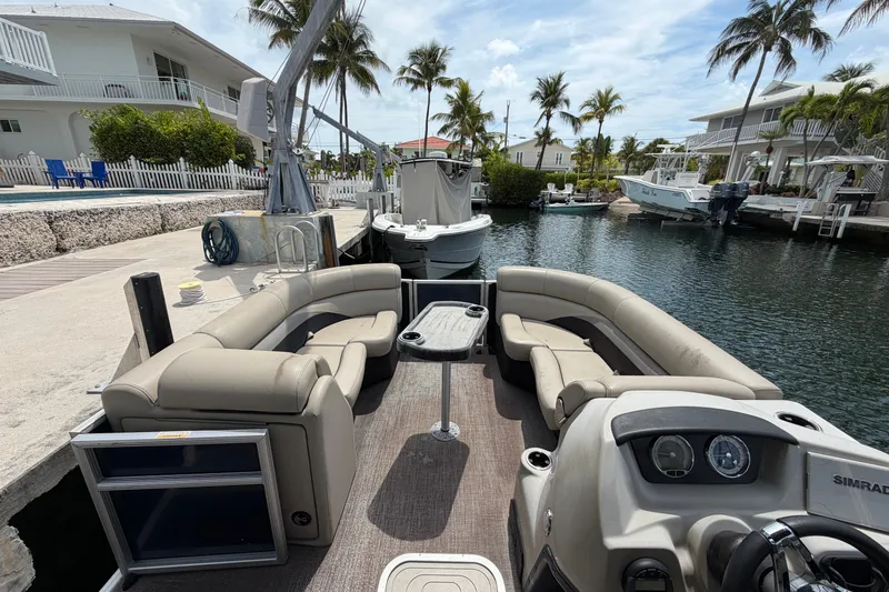 Slide: The Image of 2021 Barletta C20UC pontoon boat docked by waterfront homes and palm trees. - 2