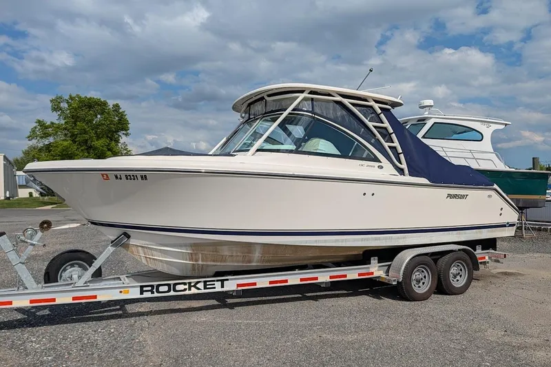 The Image of 2011 Pursuit DC 265 Dual Console boat on trailer under cloudy sky. - 0